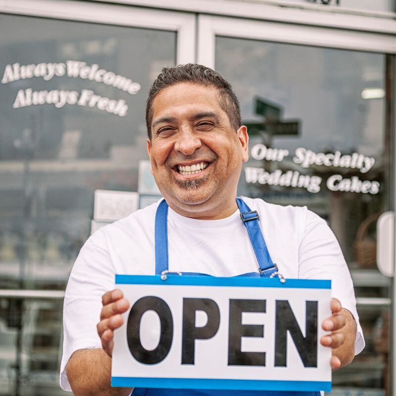 Man standing in front of a business holding an Open sign